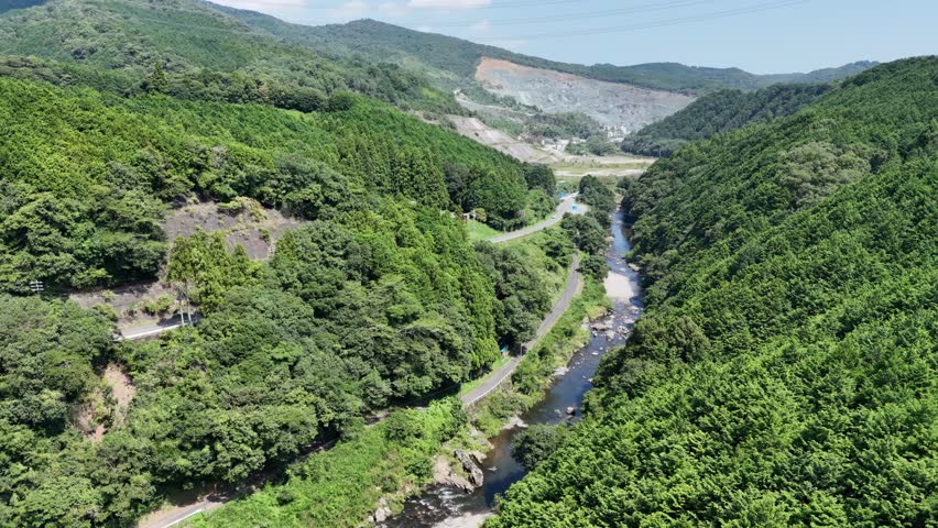 A mountain range with a river running through it. The trees are lush and green, and the sky is clear and blue. The scene is peaceful and serene, with the river flowing calmly through the valley