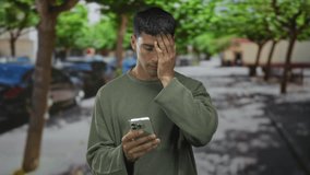 Man holding smartphone with one hand and covering face with a stress gesture in street; frustration. - Powered by Shutterstock - Get 15% off with code: PIKWIZARD15