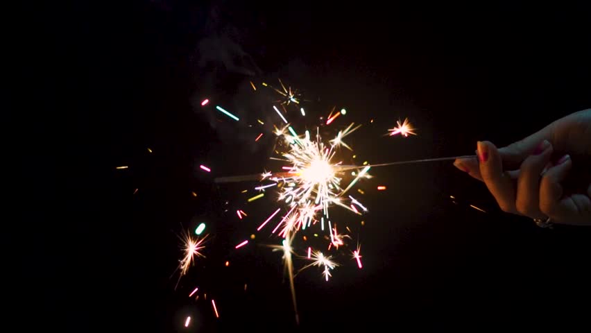 Woman hand holding a burning sparkler. Diwali, Christmas and new year sparkler background. Celebrating holidays and festival with fireworks. Burning sparkler on black background.

