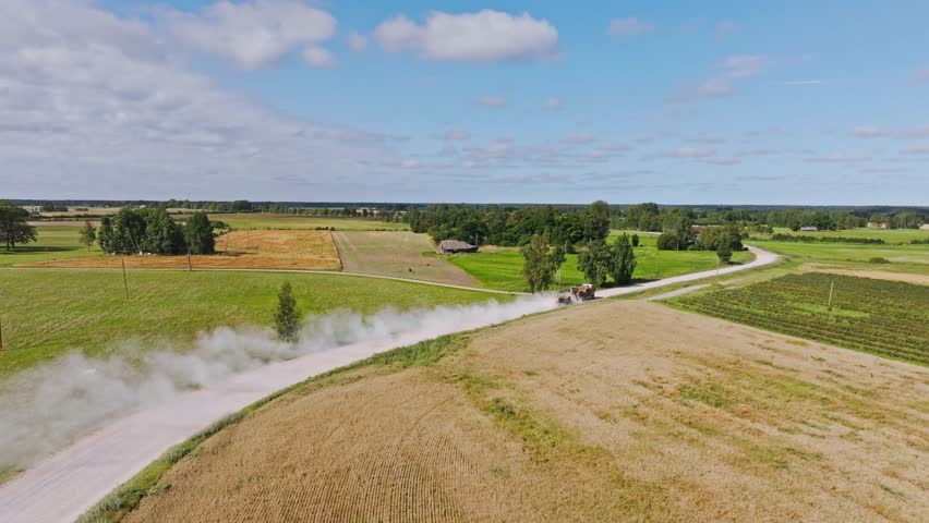 Heavy truck driving gravel road raising dust clouds over fields, drone cinematic
