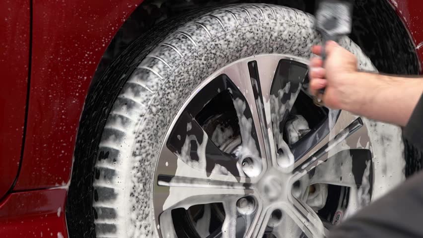 Cleaning car tyre with snow foam and tyre brush - medium close