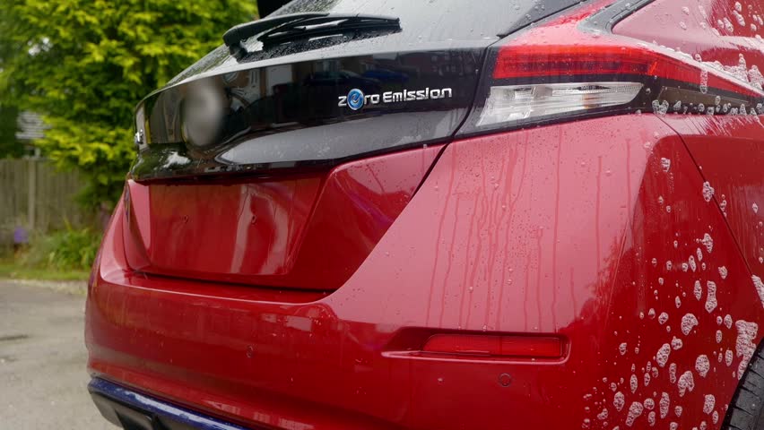Applying iron fallout remover with red and white pressure sprayer to a red EV car