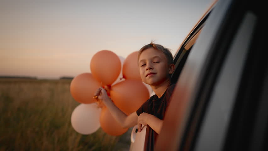 Portrait of cute 6-years-old boy with balloons traveling by car with family. Weekend trip and celebration of birthday party in nature, little dreamer dreaming of future, enjoy simple life and summer