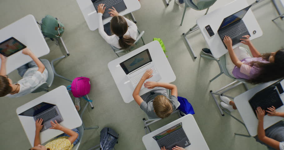 Children Sit at Desks Using Laptops, Surrounded by Luminous Digital Lines Symbolizing Virtual Connection and AI Collaboration. Technology Integration, and Future Focused Learning. Rotating Top View.