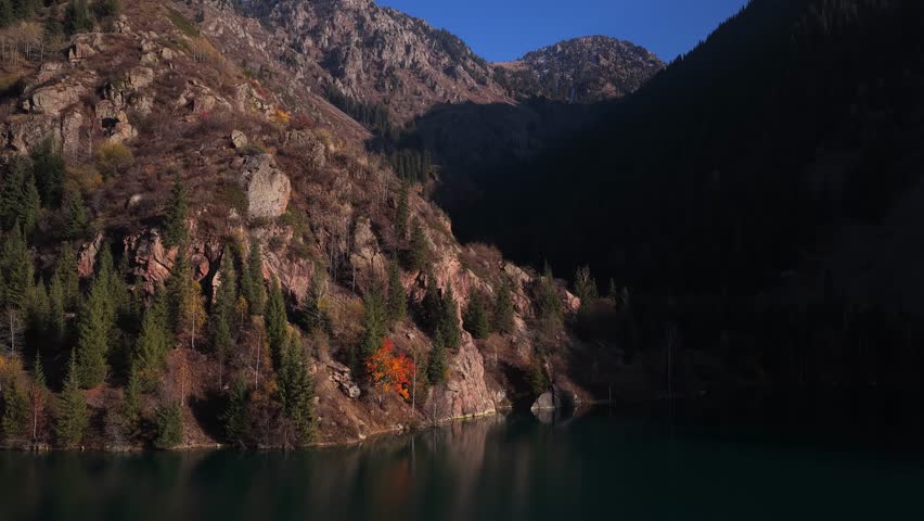 Lake Issyk in the rays of the setting sun. National Nature Park. Mountainous area with different vegetation. View from a drone. 