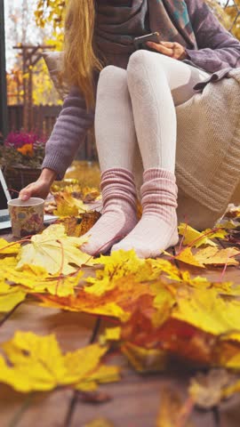 Cozy autumn morning on a wooden terrace with warm socks, blanket, and coffee. Peaceful fall mood, golden leaves, soft light, sweater weather lifestyle and comfort in nature.