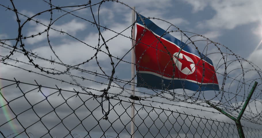 North Korea waving flag on country border concept. Korean blowing banner with barbed wire fence.