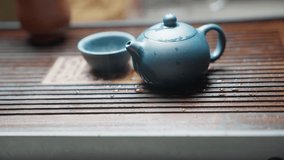 Slow motion side view: closed blue clay teapot on a bamboo tea tray emits steam as water evaporates, with a blurred blue clay teacup in the background. - Powered by Shutterstock - Get 15% off with code: PIKWIZARD15