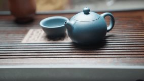 Slow motion side view: hot water is poured over a closed blue clay teapot on a bamboo tea tray, enveloping the teapot and instantly evaporating to steam, with a blurred blue clay teacup in the backgro - Powered by Shutterstock - Get 15% off with code: PIKWIZARD15