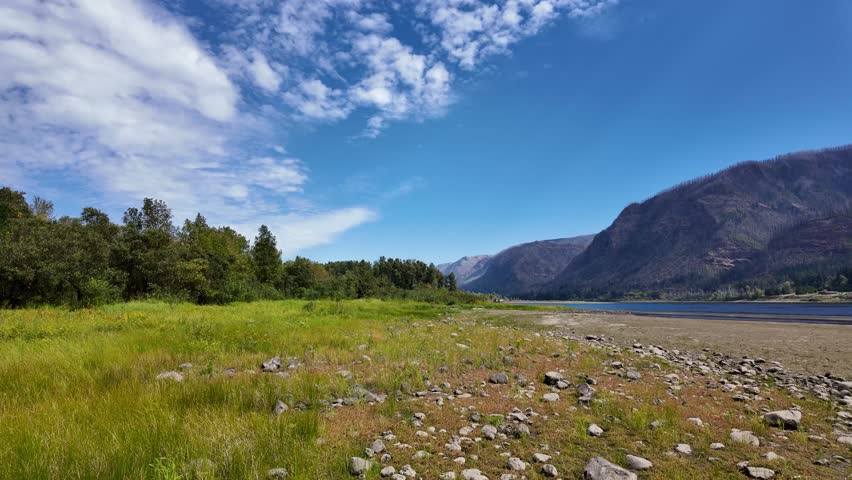 4K footage of Columbia River seen from Doetsch Day Use Area near Skamania, Washington, USA. Peaceful nature scene with blue water, mountains,  forested shoreline in early fall season under clear sky