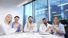 Group of doctors applauding look at camera sitting in a hospital office boardroom celebrate success. Happy medical professional physicians in white coats diverse team colleagues rejoice achievement - Powered by Shutterstock - Get 15% off with code: PIKWIZARD15