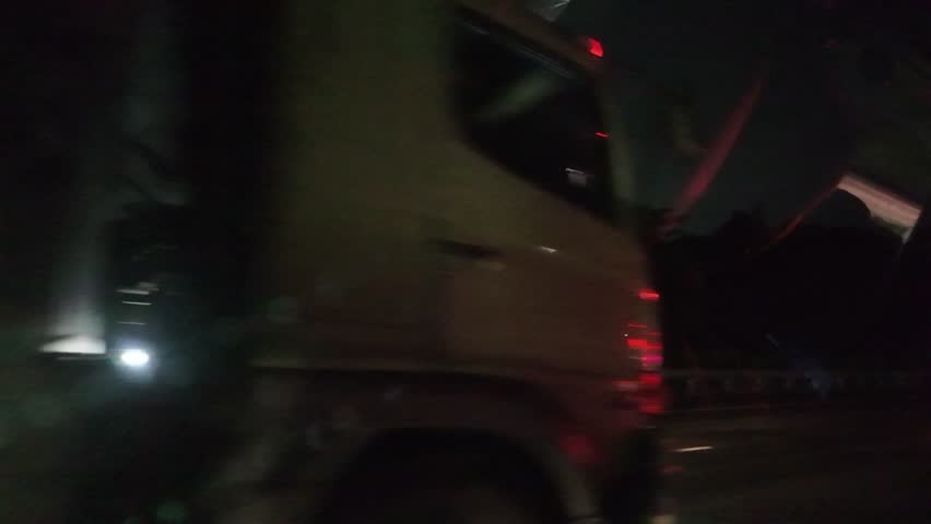 A large truck drives on a road at night. The truck appears to be transporting goods. The scene is dark with limited visibility.