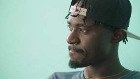 Close up of young man turning head toward camera after staring pensively, lost in thought, wearing cap backwards, showing contemplative expression on face against teal background in soft light - Powered by Shutterstock - Get 15% off with code: PIKWIZARD15