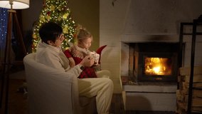 Cozy winter evening by the fireplace - grandmother and grandson share warm tea and cookies near a glowing Christmas tree. Peaceful family holiday moment filled with love, comfort, and festive lights. - Powered by Shutterstock - Get 15% off with code: PIKWIZARD15