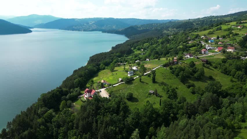 Cinematic drone footage flying backward over Bicaz Lake in Romania, revealing calm waters, forested mountains, and stunning natural scenery.