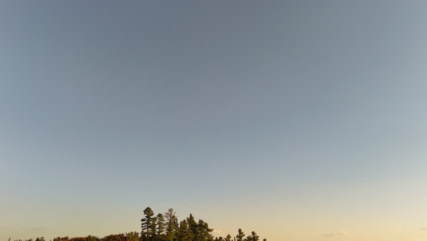 Aerial view of a colorful autumn sunset over a lake and forested mountains in Mauricie, Quebec, Canada. Warm golden light reflects on the calm water.