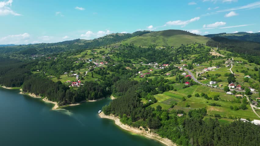Aerial backward drone shot over Bicaz Lake, Romania, showing blue water, green hills, and scenic mountain views.