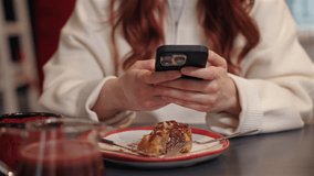 Close-up of female hands holding smartphone above half-eaten dessert and fork. Browsing content or chatting online with friends. Relaxing at cafe table after enjoying sweet pastry and drink. - Powered by Shutterstock - Get 15% off with code: PIKWIZARD15