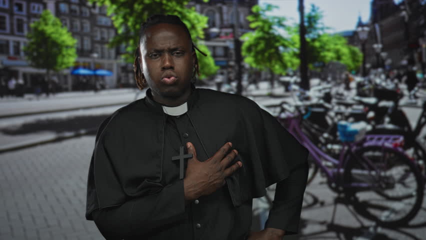 Man priest with hand on chest holding wooden cross, wearing clerical collar on busy city street with bicycles and trees; devotion prayer.
