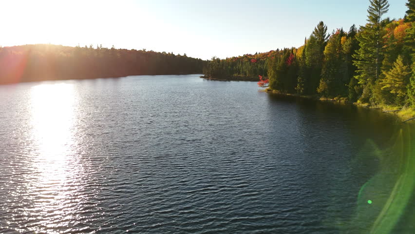Aerial drone view of a colorful autumn sunset over a forest and lake in Mauricie, Quebec, Canada. The warm light enhances the vivid seasonal tones.