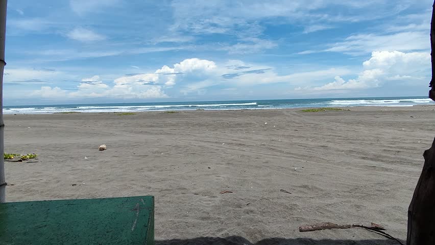 Serene Dark Sand Beach View with Rolling Waves and Cloudy Blue Sky