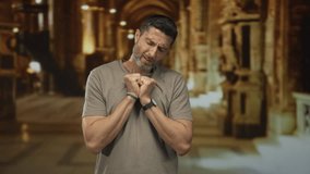 Man praying with clasped hands in church, eyes closed and humble expression, wearing a watch and bracelet, tshirt visible; devotion reflection hope. - Powered by Shutterstock - Get 15% off with code: PIKWIZARD15