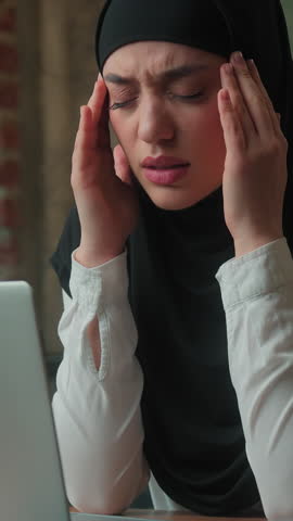 Tired ethnic Eastern Hindu business woman muslim businesswoman in hijab female exhausted overworked sick girl islamic entrepreneur with laptop feeling headache holding painful head in office tension