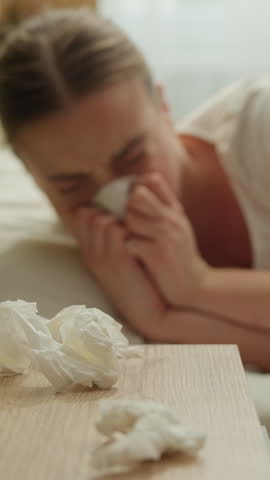 Suffering Caucasian sick woman sneezing lying in bed with runny nose tissue female suffering cold flue symptoms girl illness health problem seasonal virus rest fatigue healthcare sneeze throw napkin