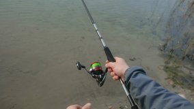Fisherman hands and dog reeling in line on spinning rod and reel while fishing from the riverbank, showcasing the angling technique from an immersive first person perspective - Powered by Shutterstock - Get 15% off with code: PIKWIZARD15