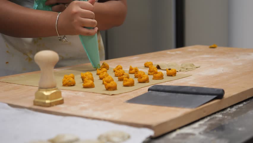 Fresh pasta dough being prepared with delicious butternut squash filling for tortelli ravioli being made by hand in a kitchen setting of a small business in Emilia Romagna Italy
