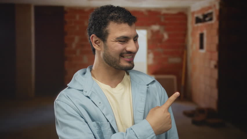 Man wearing light blue jacket smiling and giving thumbs up in building; confidence optimism motivation ambition.