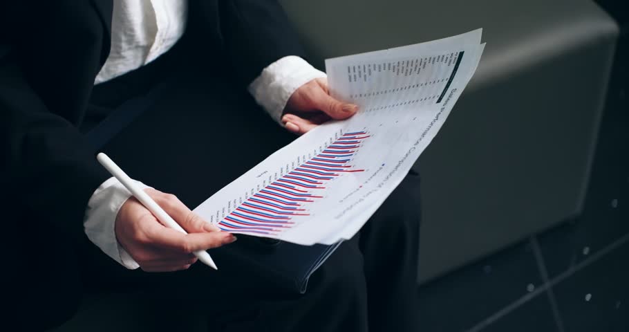 A slow motion parallax close-up shot glides past a businesswoman's hands as she analyzes a financial bar graph, pointing to the data with a stylus