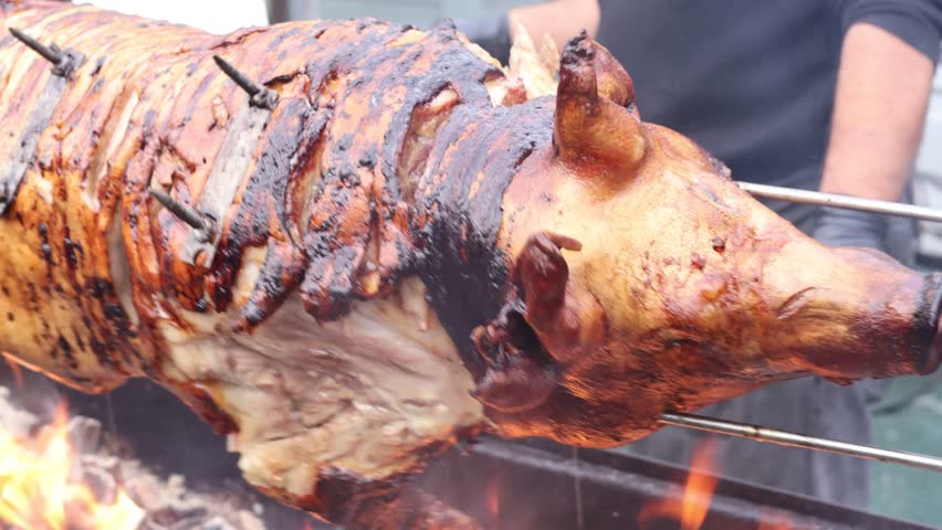 Whole piglet roasting on a skewer over open fire, crispy golden skin and juicy meat, traditional outdoor barbecue