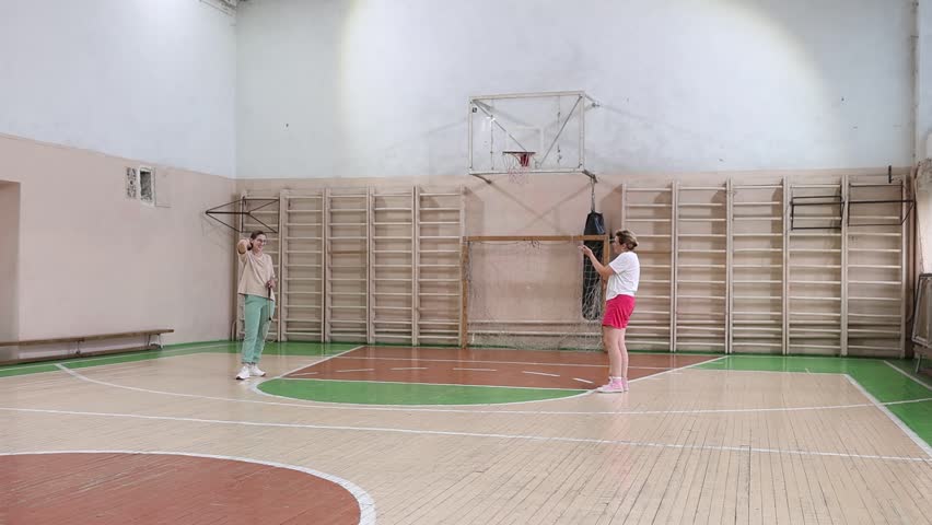 Two women playing badminton in a gym with a wooden floor.