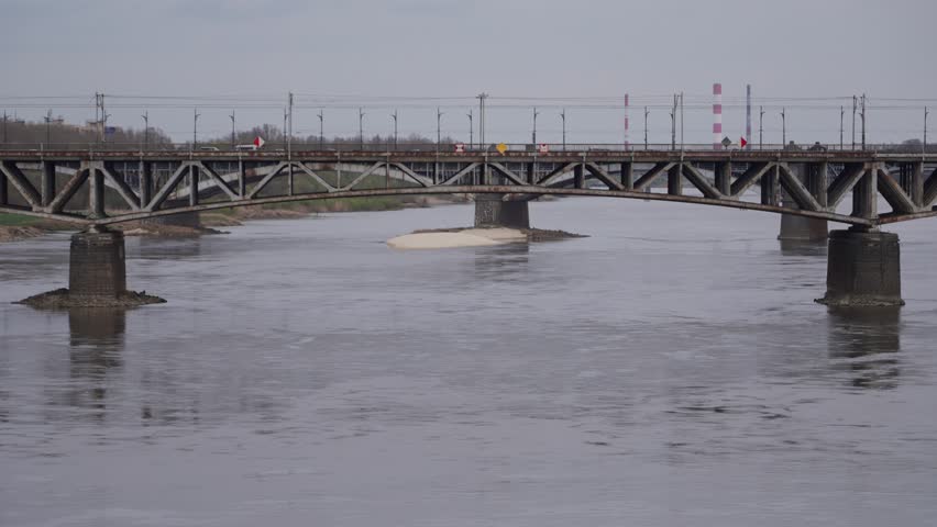 A train crosses a railway bridge over a river. Trains crossing the Srednicowy Railway Bridge over the Vistula River. Warsaw, Poland.