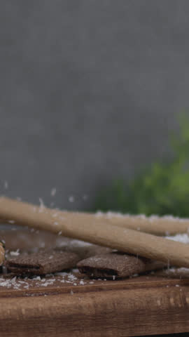 Pouring dark molten chocolate over a vanilla cupcake topped with coconut flakes, filmed in high definition on a wooden board, creating a delightful contrast of textures and flavors.