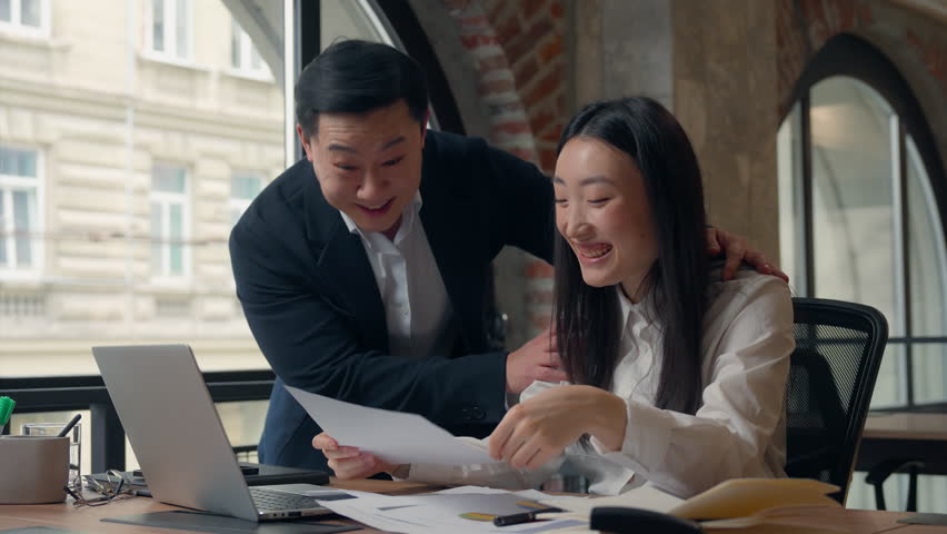 Two Korean business team coworkers celebrate financial growth shaking hands diagram success Asian businesswoman working papers Chinese boss businesswoman positive supporting satisfied showing thumb up