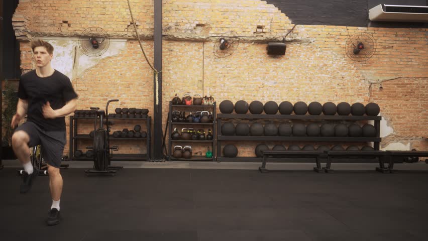 fit young man performing high-intensity knee drives during cardio interval with camera steadily pushing forward to emphasize determination