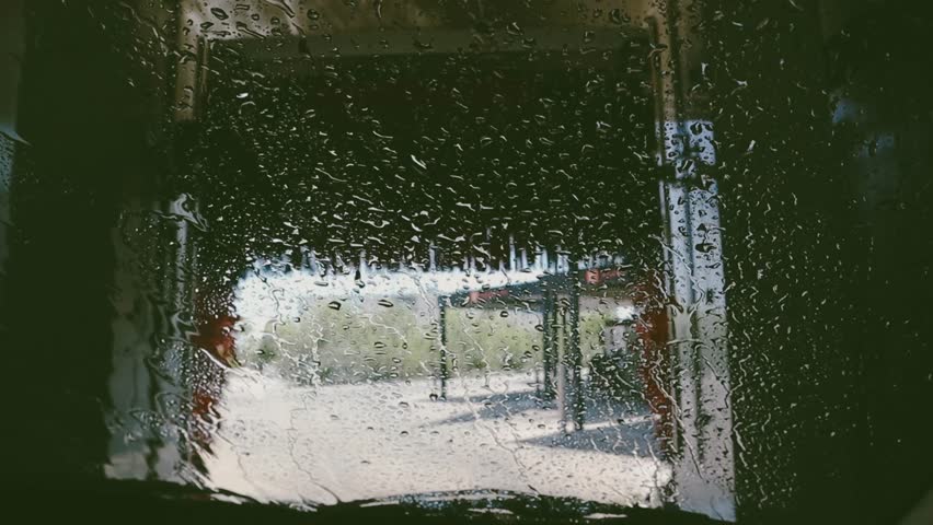 View from inside a car wash with water droplets on the windshield. The photo captures the unique perspective of a car wash experience, with water and brushes visible. Tunneling automotive wash.