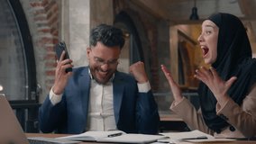 Happy Arabian business team winning with phone giving high five excited job two colleagues in office man with woman in hijab Muslim businessman with businesswoman smartphone achive victory success - Powered by Shutterstock - Get 15% off with code: PIKWIZARD15
