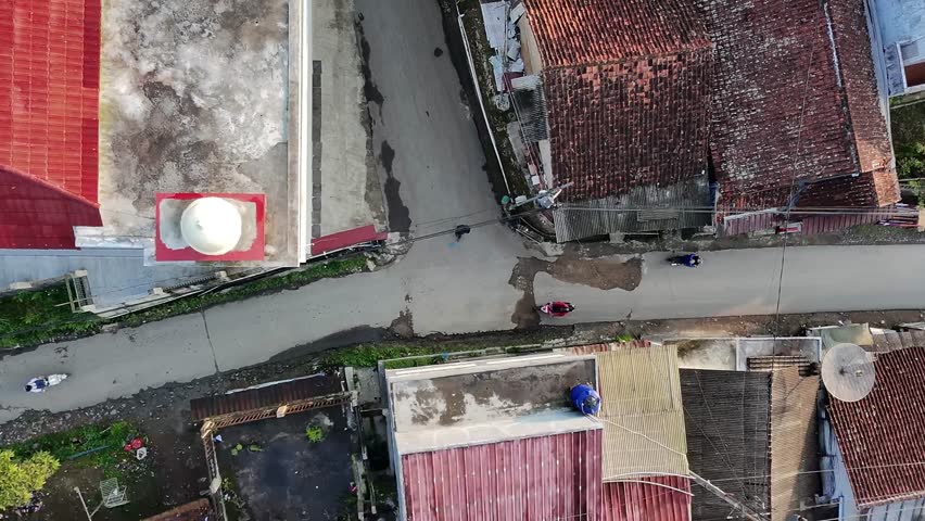 Aerial top view of an urban neighborhood intersection with motorcycles, rooftops, and narrow streets, showing everyday life in a small residential area