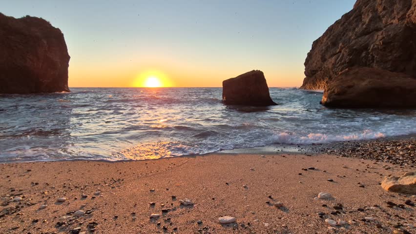 Sunset Beach Ocean Waves washing sandy shore with large rock formations at golden hour, tranquil natural landscape
