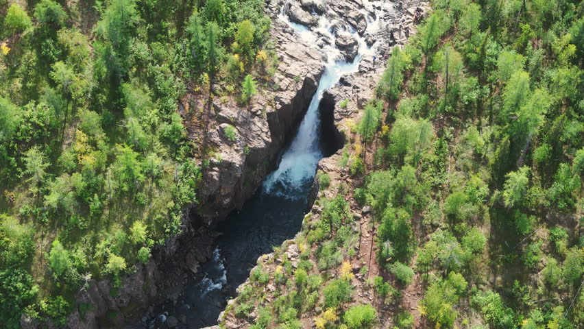 Top down look at a powerful cascade tearing through a steep rock gorge near Lake Lama on the Putorana Plateau in Russia. Midday light and blue water with taiga forest highlight a travel destination