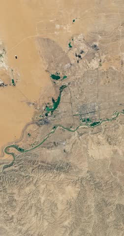 Flying above small town in dry desert area among sands. Camera is zooming out, rotating counterclockwise. Vertical video. Animation based on image by NASA