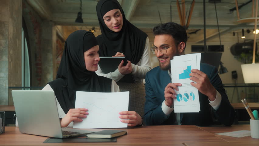 Muslim business team presenting data stats on video call laptop meeting in office three partners Arabian businesswomen in hijab Indian businessman showing documents growth financial graphs negotiation - Powered by Shutterstock - Get 15% off with code: PIKWIZARD15