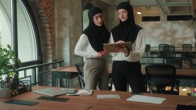 Two Islamic business women team negotiate discuss project talking in office creative businesswomen arabian muslim girls female in hijab looking at digital tablet gadget pointing in front corporate job - Powered by Shutterstock - Get 15% off with code: PIKWIZARD15
