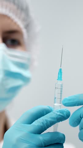 A healthcare professional wearing gloves and a mask holds a syringe ready for vaccination in a sterile environment.