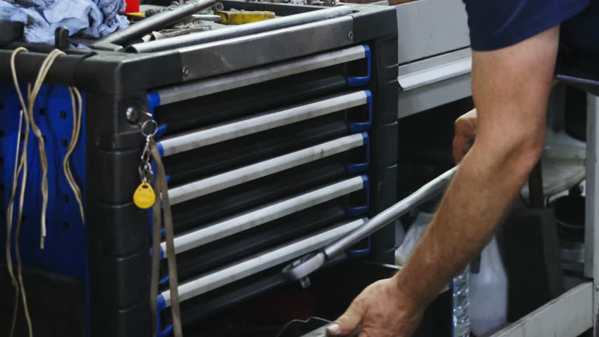 Technician places wrench and parts in drawer of toolbox in workshop closeup. Mechanic hides instruments in chest organizer in garage