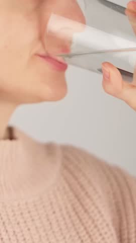 Vertical close-up of an unrecognizable woman drinking a glass of water. Concept of hydration, daily routine and healthy lifestyle.
