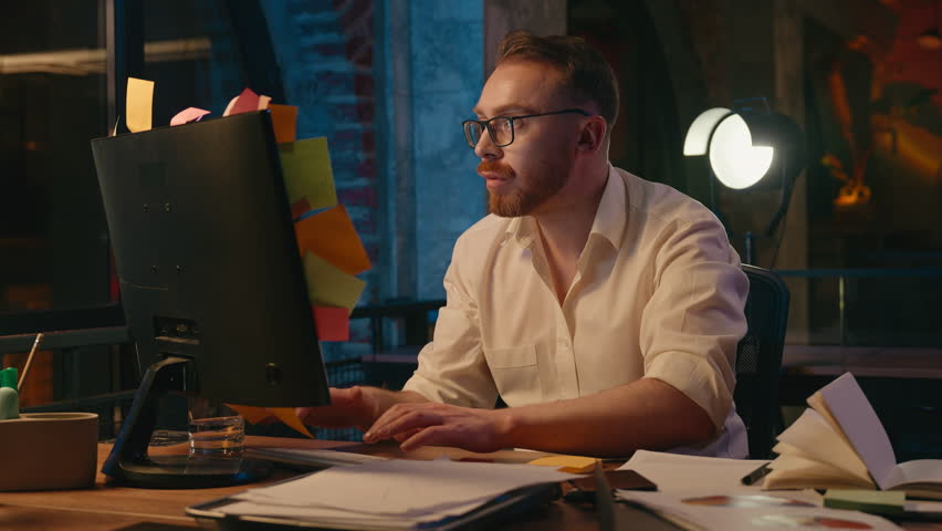Irritated Caucasian business man at night throwing away stickers from monitor office computer stressed exhausted overworked businessman male guy check throw sticky notes with work tasks holding head